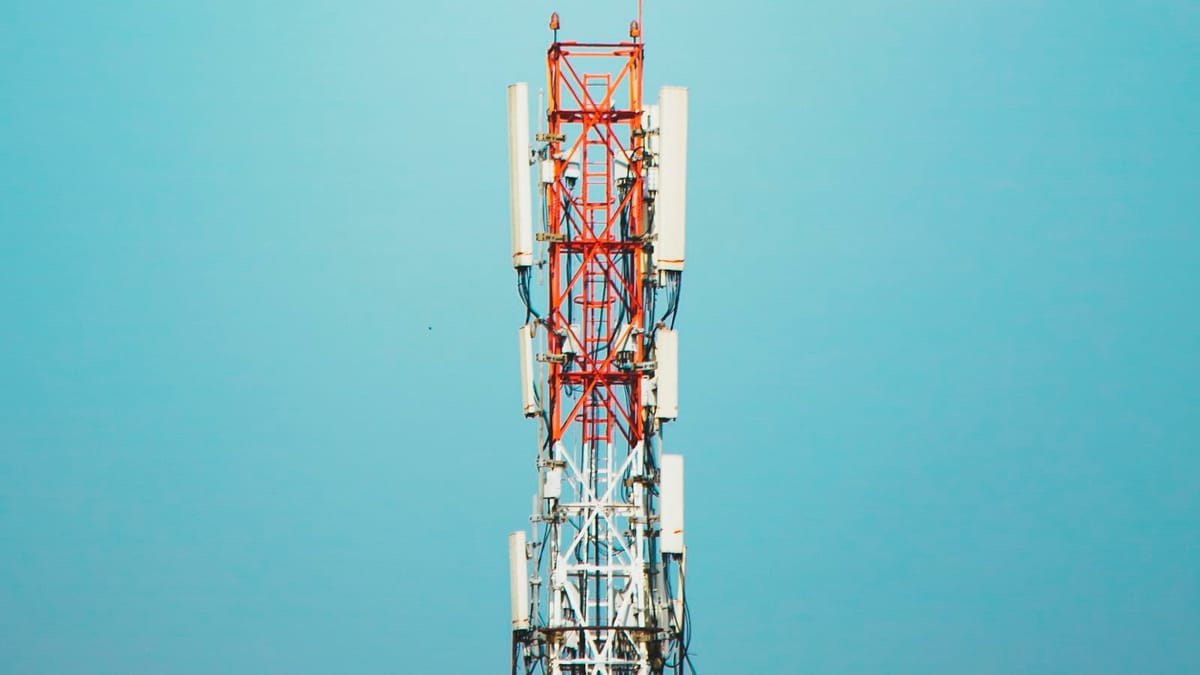 Red and white telecom tower with cellular antenna panels against a clear blue sky