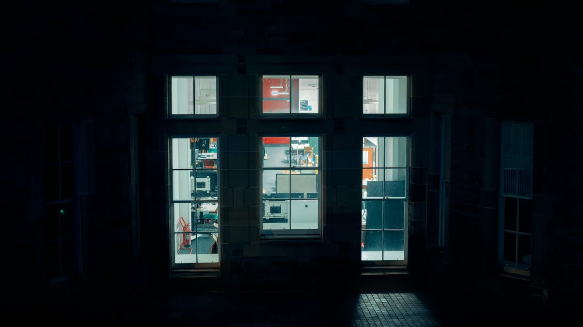 Three lit windows of a lab building at night, seen from a dark courtyard